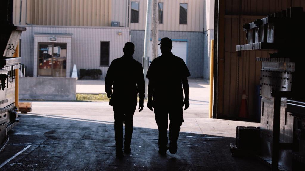 two men in silhouette walking out of a garage.